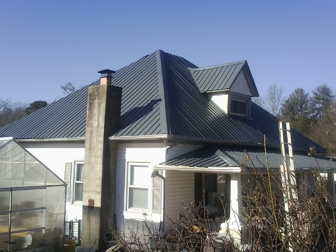 Dark blue standing seam metal roof on a white farmhouse with dormer — Slate & Tile Roof Repair by Roofing Brothers in Martelle