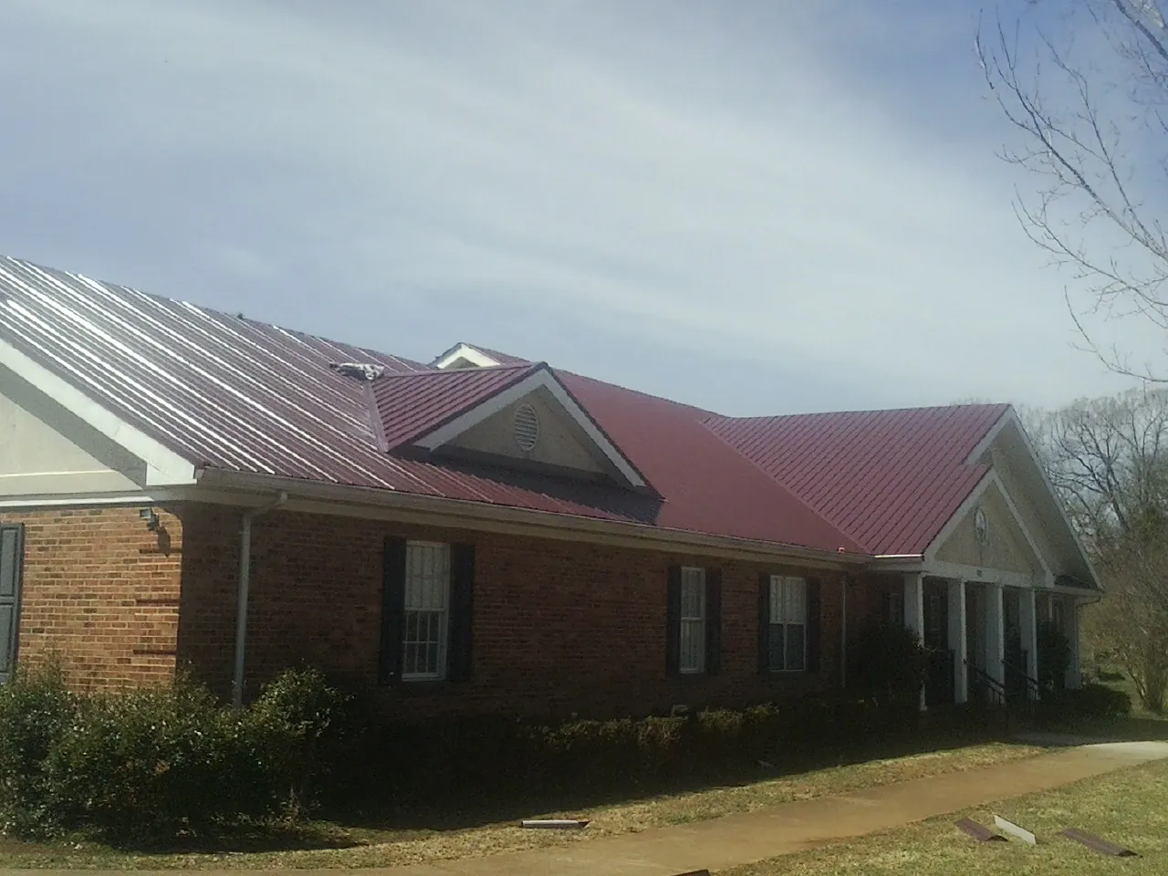 Red metal roof with gabled entries on a long brick building, from a Hail Damage Roof Repair job in Martelle