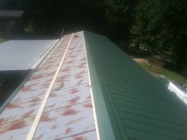 Old rusted panels beside newly installed green metal roofing — Wind Damage Roof Repair by Roofing Brothers in Martelle