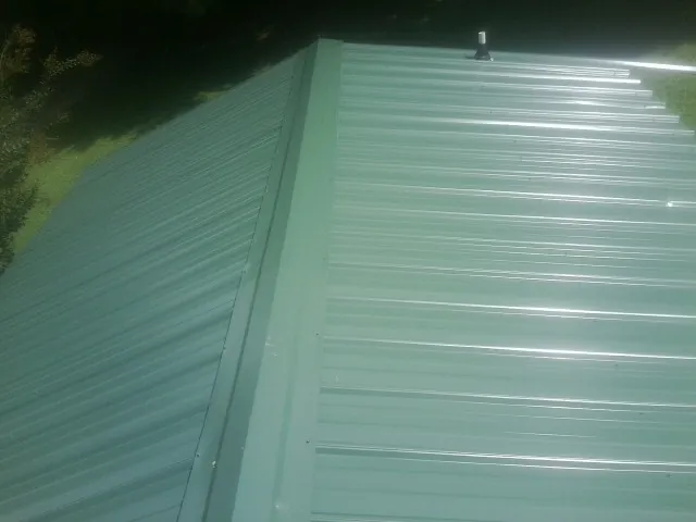 New green metal panels meeting at the ridge of a roof — Flat Roof Repair work by our crew in Martelle