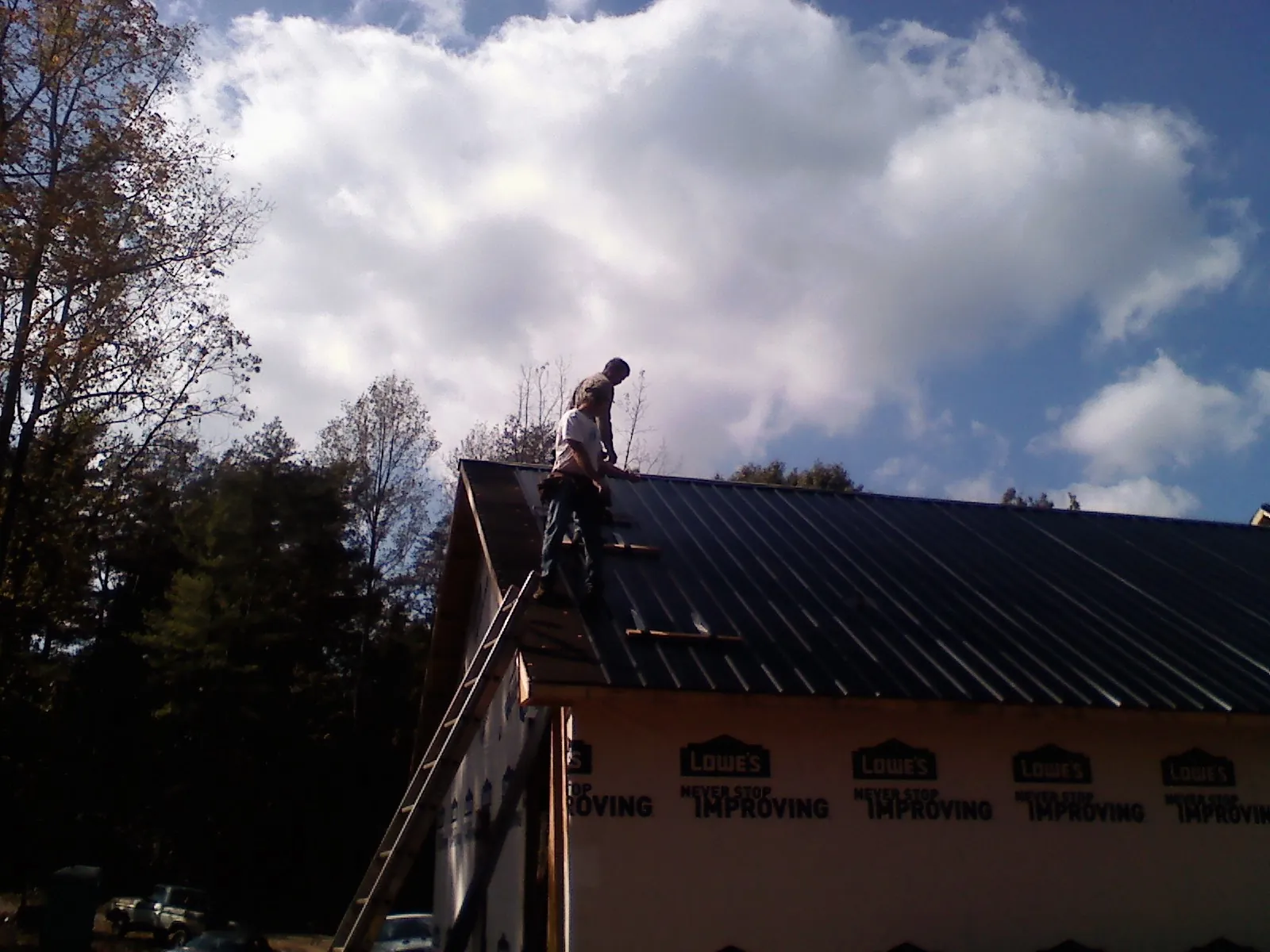 Roofer fastening dark metal panels high against a cloudy sky, from a Roof Inspection job in Martelle