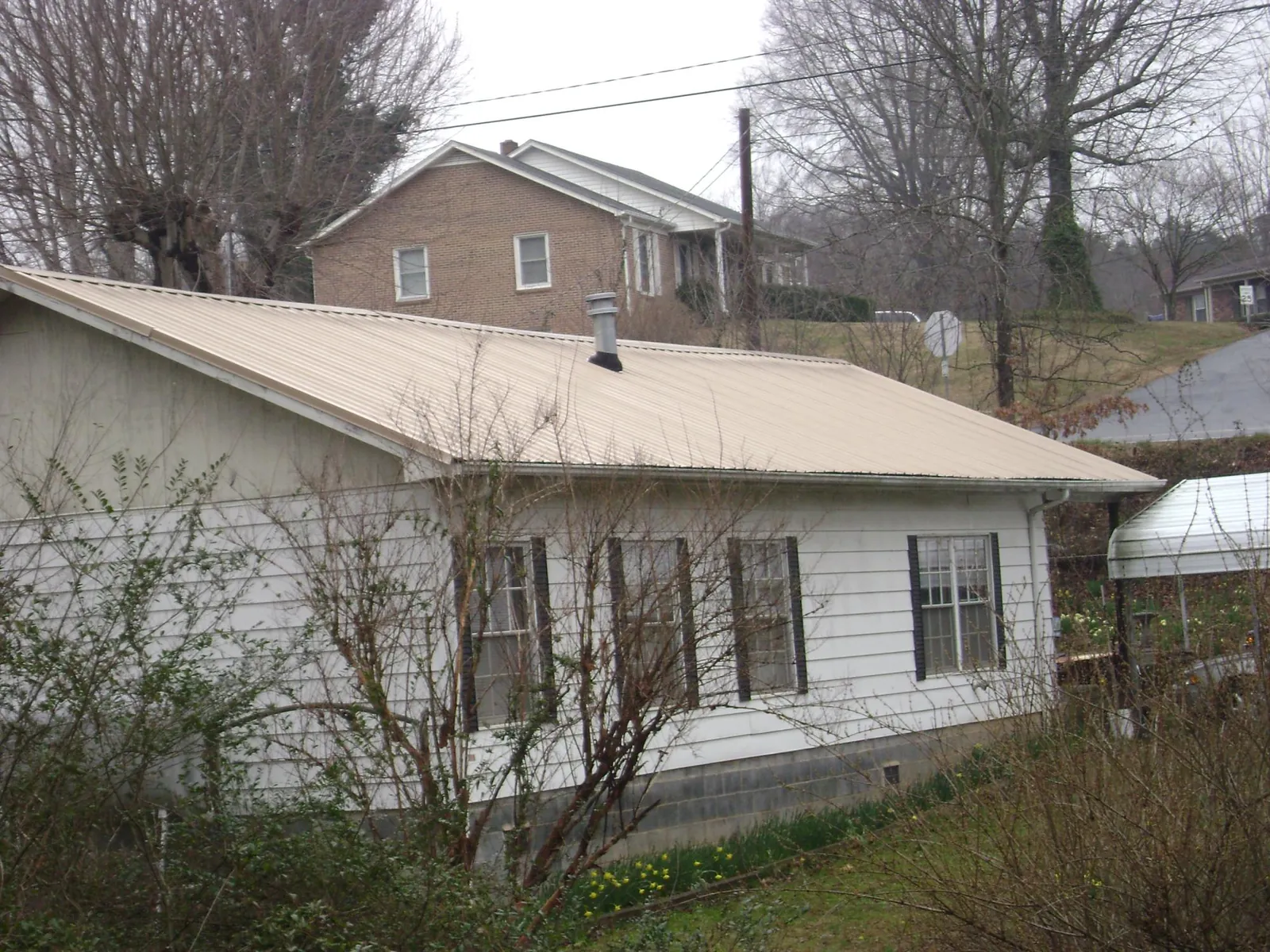 Tan metal roof on a white sided house set into a hillside — Commercial Roofing by Roofing Brothers in Martelle