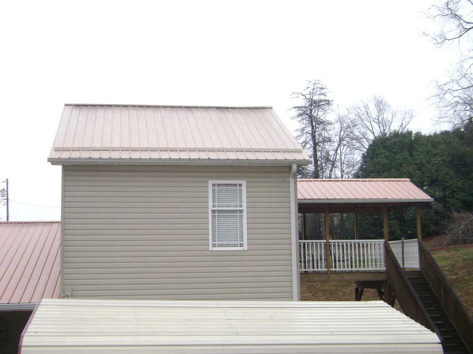 Tan metal roofs on a two story addition and attached porch, from a Roof Replacement job in Martelle